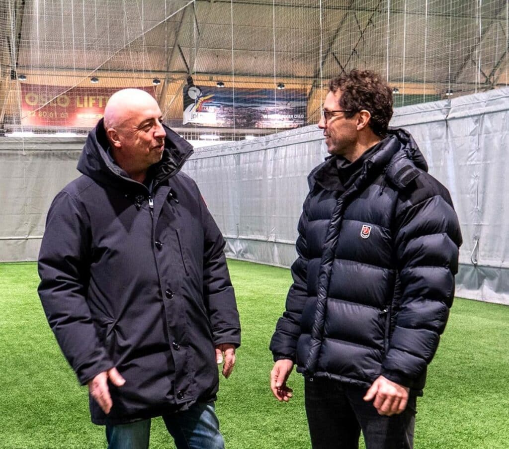 Per Einar Karlsen i Norsk Tipping og Freddy Dos Santos snakker med hverande ute på en stadion