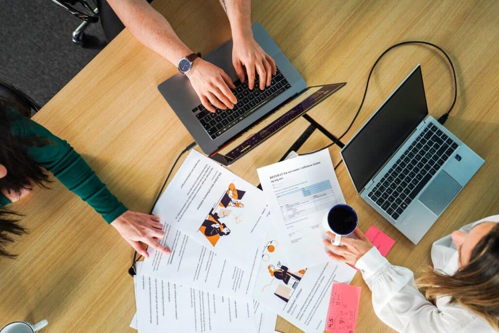 Illustrasjonsfoto som viser hender som jobber på pc, ark på bordet med referat fra styremøte. Bildet illustrerer styrearbeid.